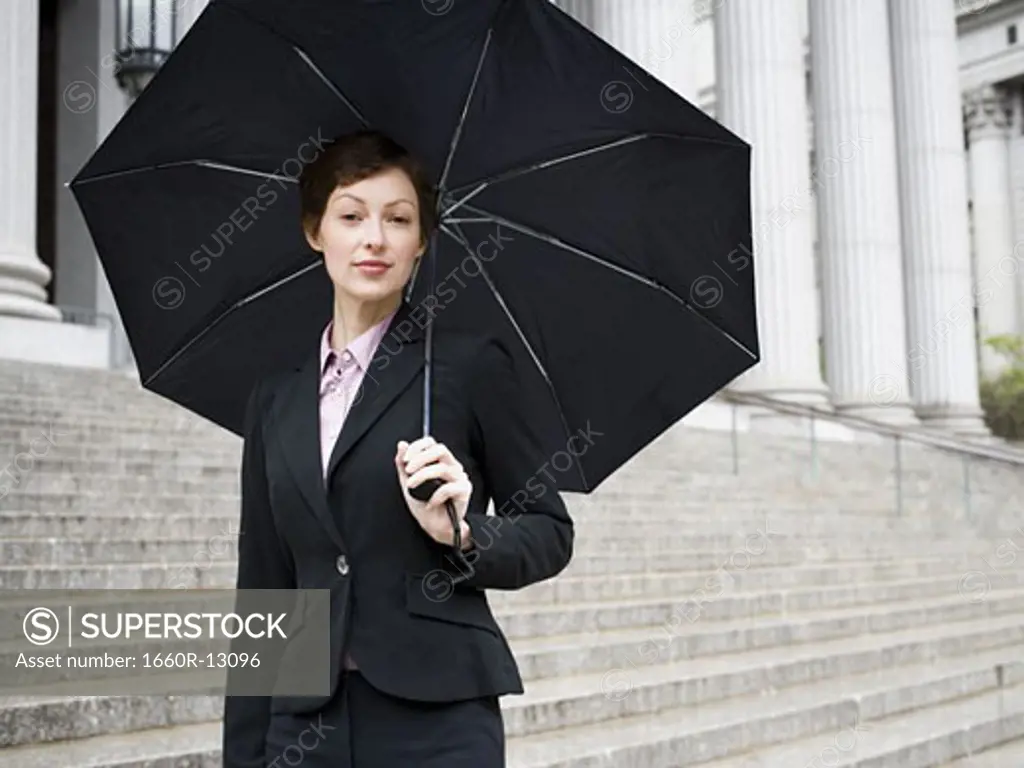Portrait of a female lawyer standing on the steps of a courthouse and holding an umbrella