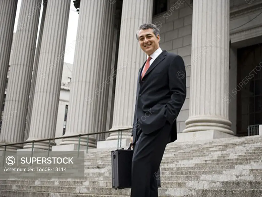 Low angle view of a male lawyer standing on the steps of a courthouse and smiling