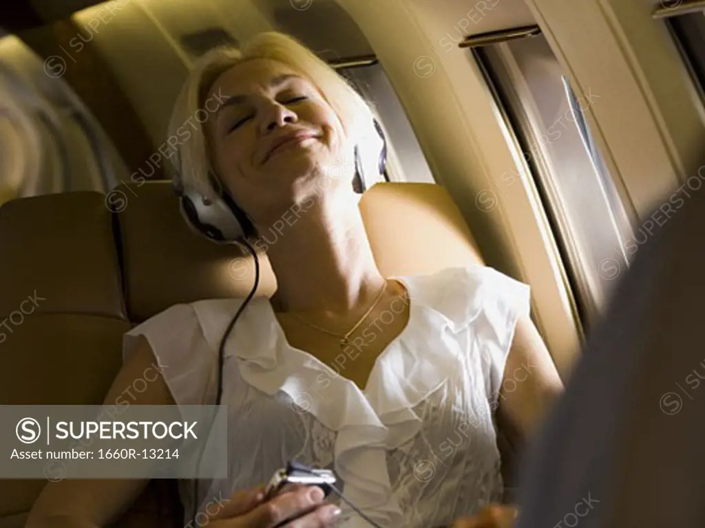 A businesswoman listening to music on headphones in an airplane