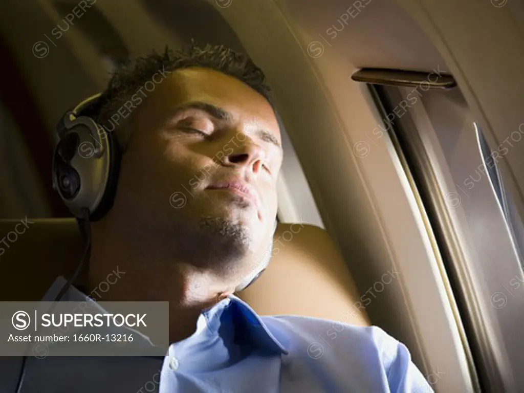 Close-up of a businessman sleeping and  listening to music on headphones in an airplane