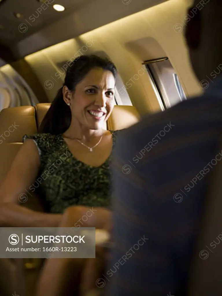 A businesswoman looking at a businessman and smiling on an airplane