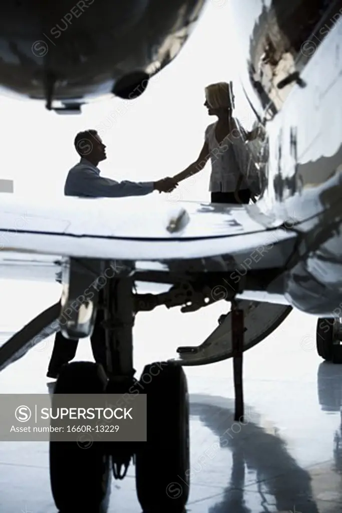 Businessman shaking hands with a businesswoman stepping down from an airplane