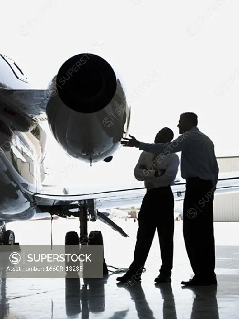 Two businessmen looking at a jet engine on an airplane