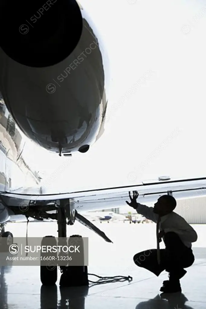 Businessman crouching and inspecting an airplane wing