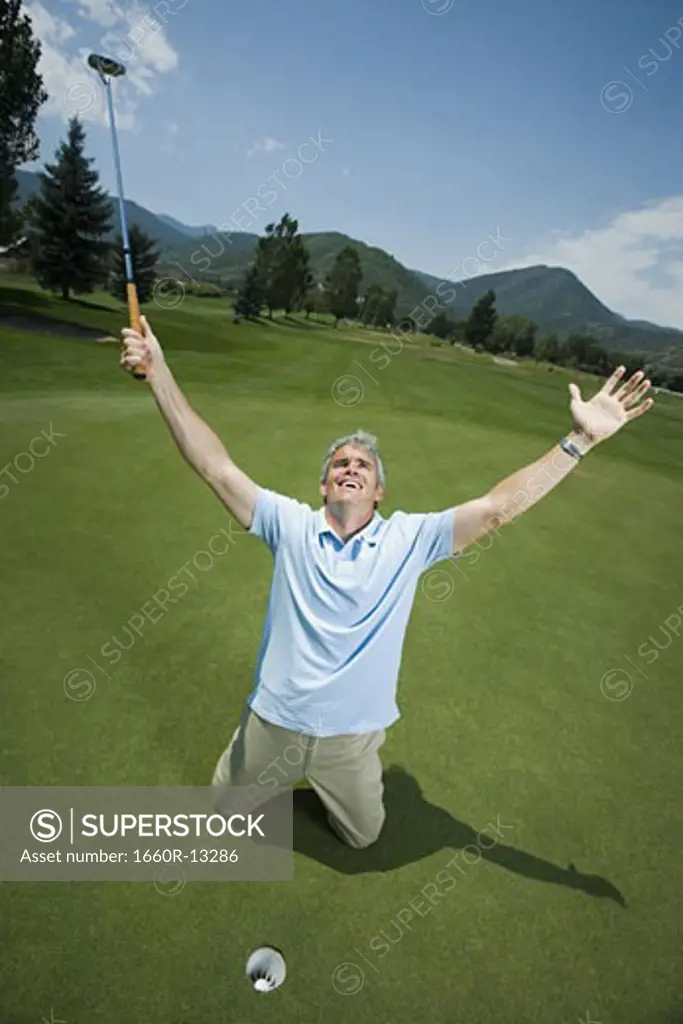 Man kneeling near a golf hole with his arms raised