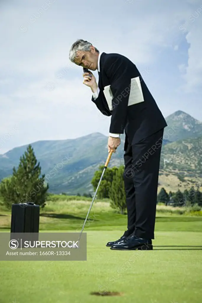 Profile of a businessman playing golf and talking on a mobile phone