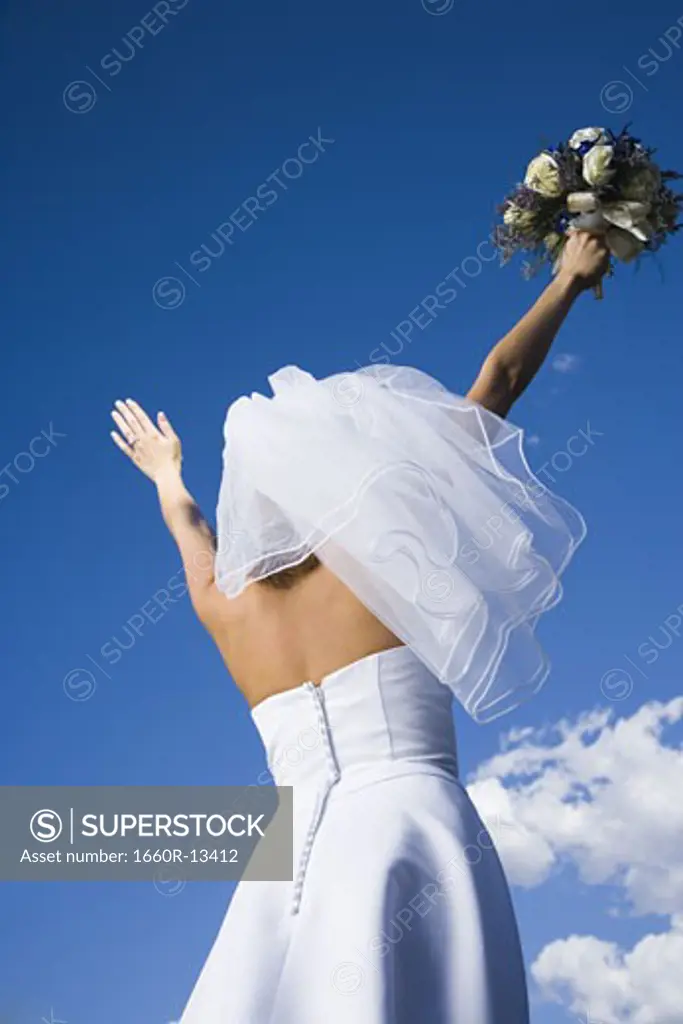 Low angle view of a bride holding a bouquet of flowers with her arms raised