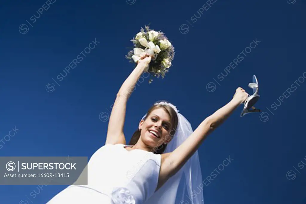 Portrait of a bride holding a bouquet of flowers and a pair of sandals