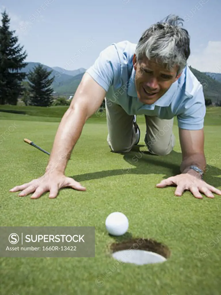 Close-up of a man kneeling on a golf course and looking at a golf ball