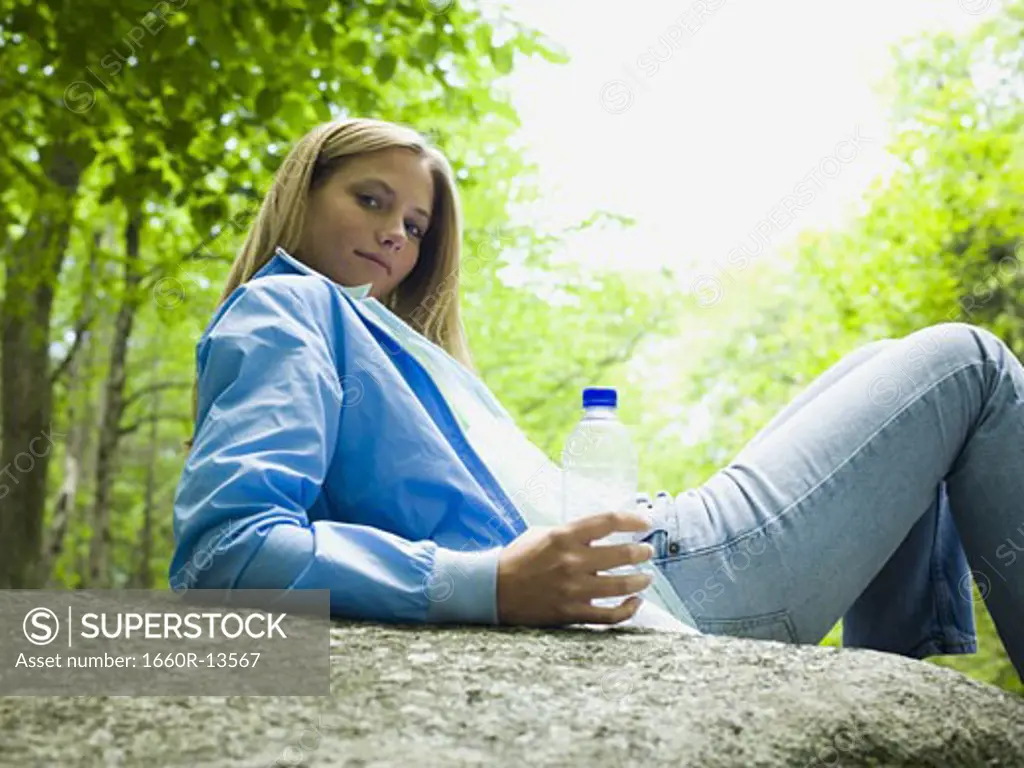 Portrait of a young woman lying on a rock and holding a water bottle