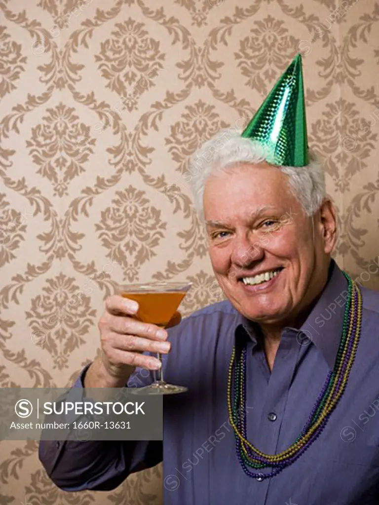Portrait of a senior man holding a glass of martini and wearing a party hat