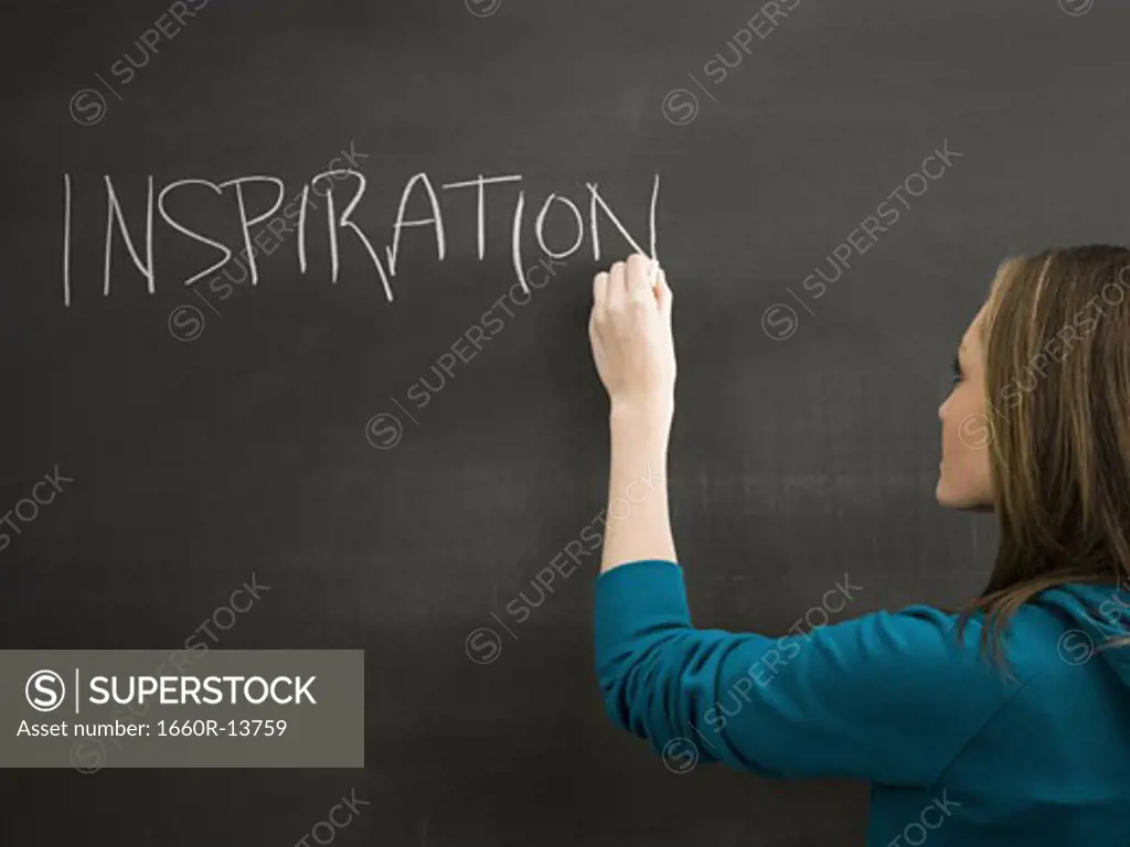 Female student writing word inspiration on chalkboard