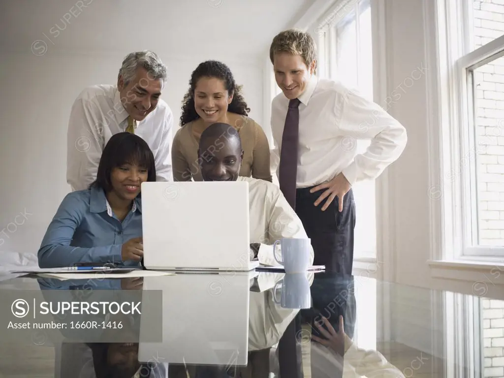 Three businessmen and two businesswomen looking at a laptop