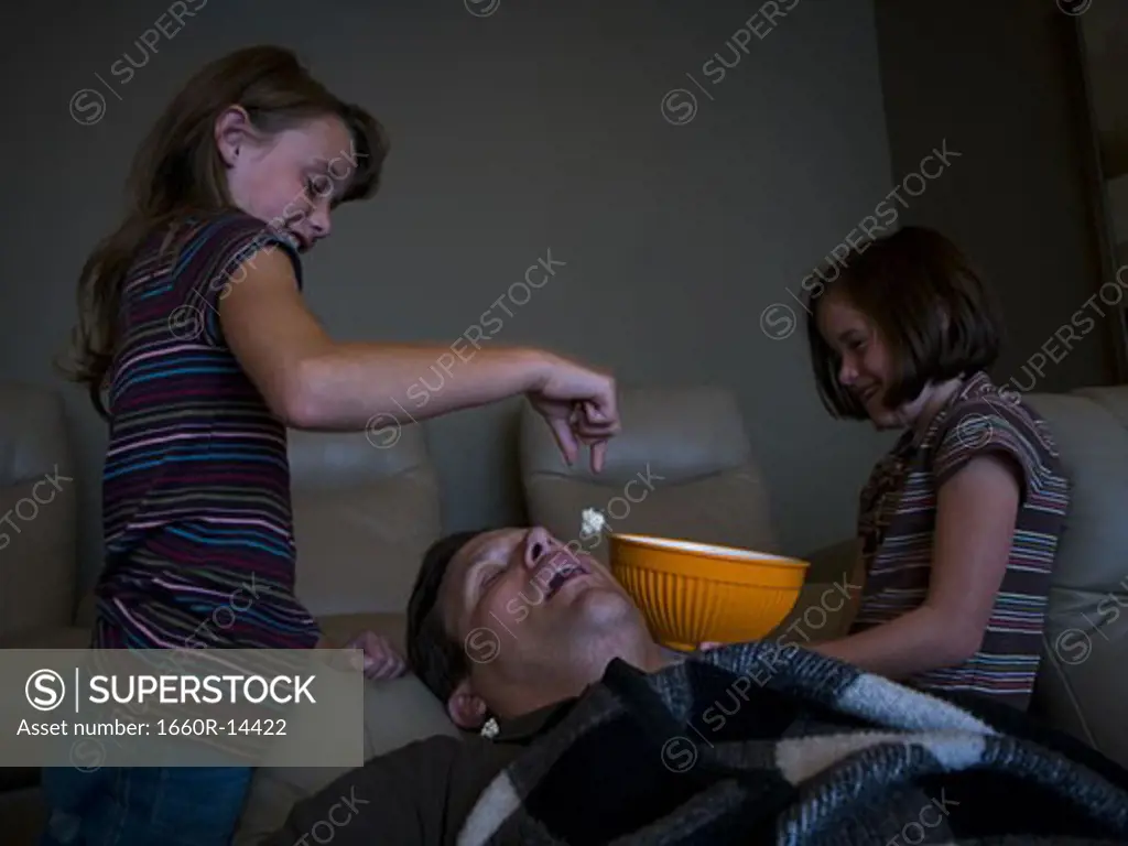 Daughters dropping popcorn into sleeping father's mouth