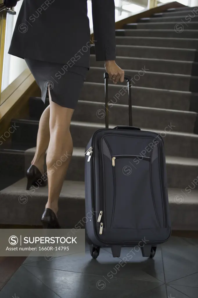 Businesswoman carrying luggage up a flight of stairs