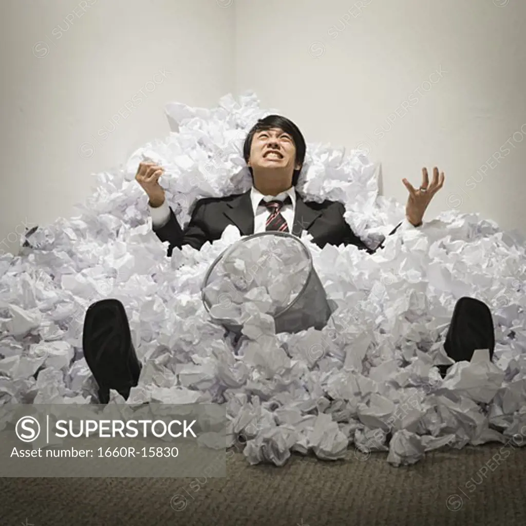 Businessman buried in mountain of crumpled papers