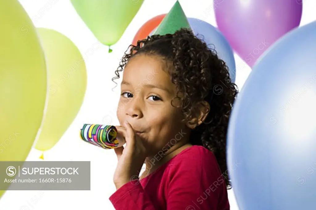 Young girl wearing party hat and playing amongst balloons