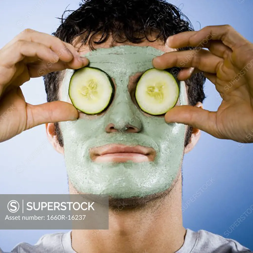 Man with mud mask and cucumber slices on eyes