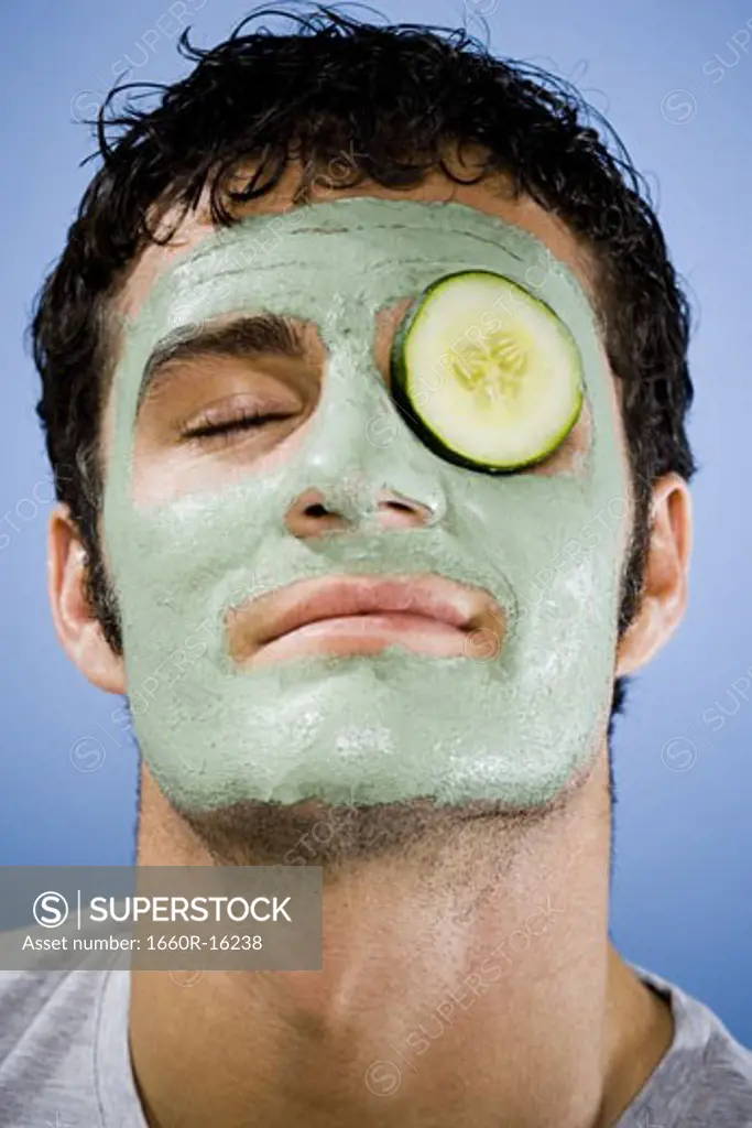 Man with mud mask and cucumber slice with closed eyes