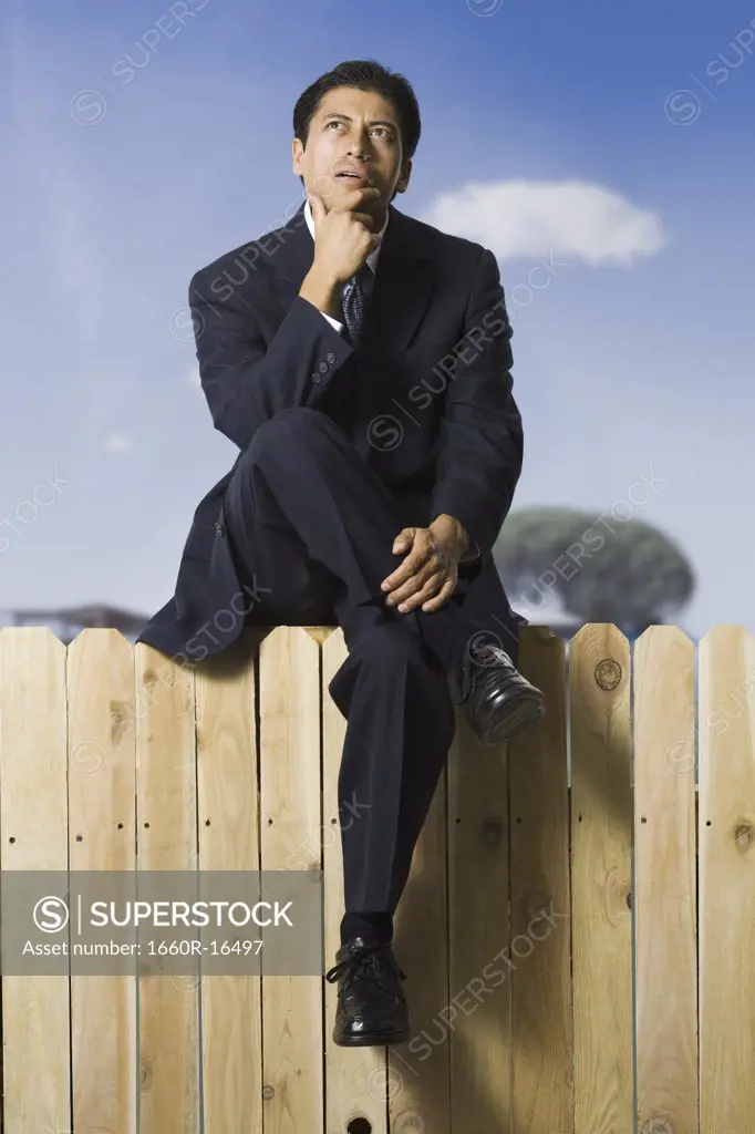Businessman sitting on fence looking up