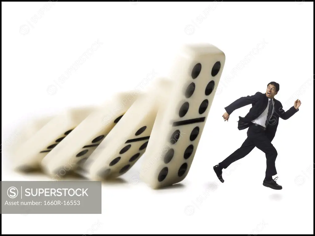 Businessman running from falling dominoes