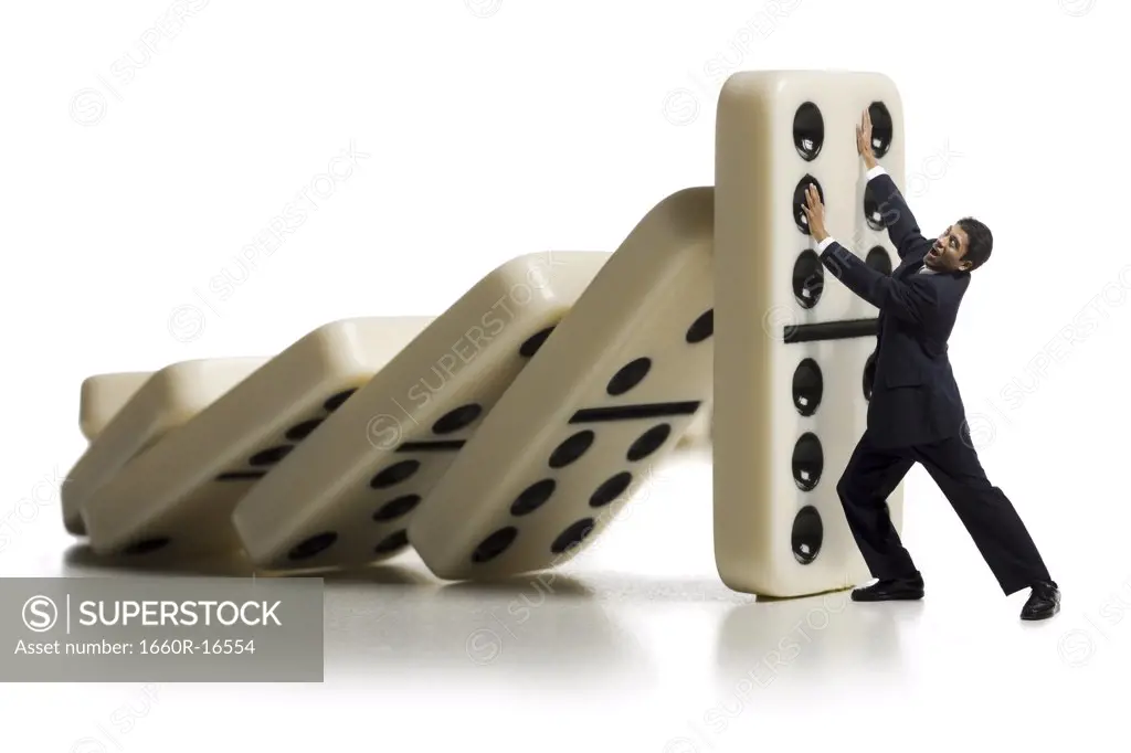 Businessman holding up falling dominoes
