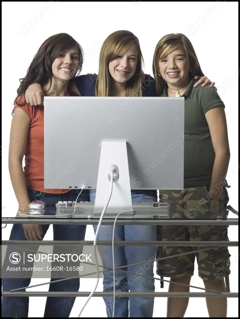 Three girls standing behind computer monitor smiling