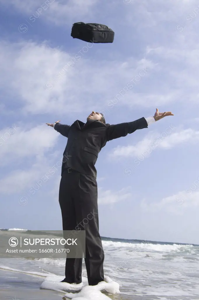 Businessman tossing briefcase in air at beach