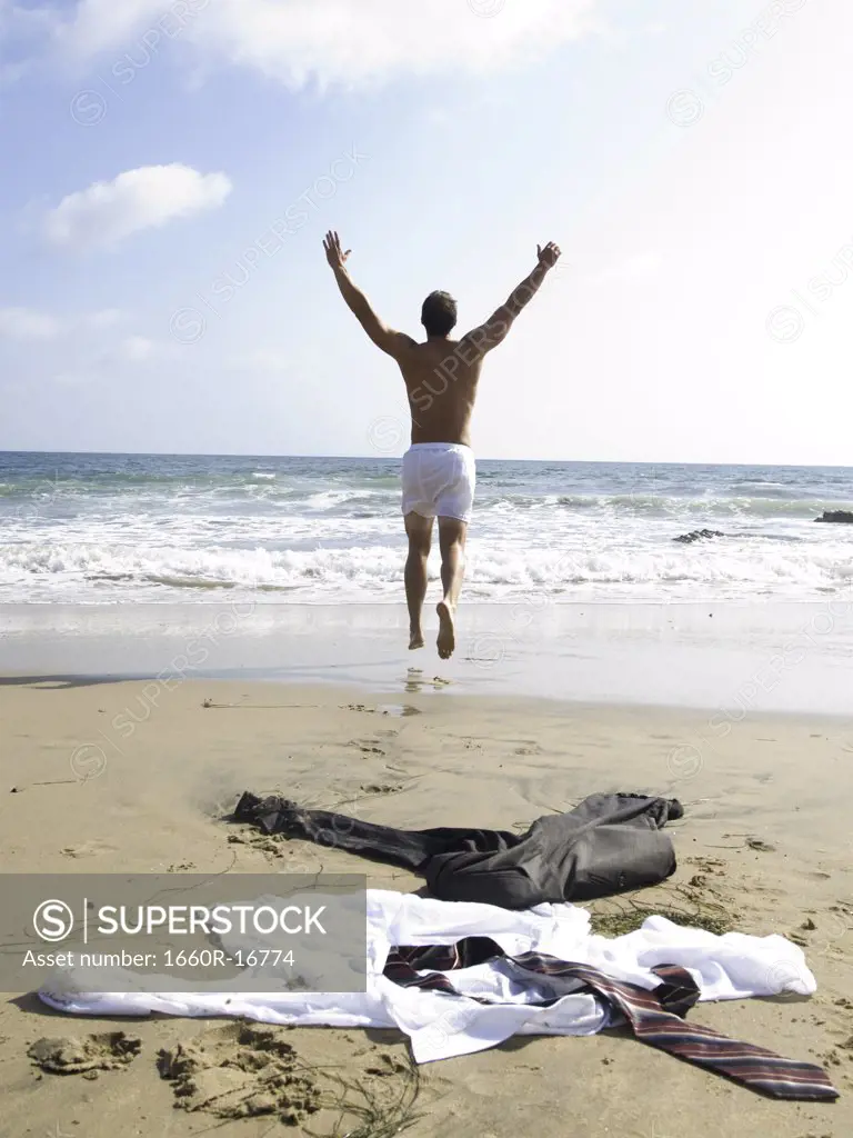 Man in underwear running to water with business attire on sandy beach