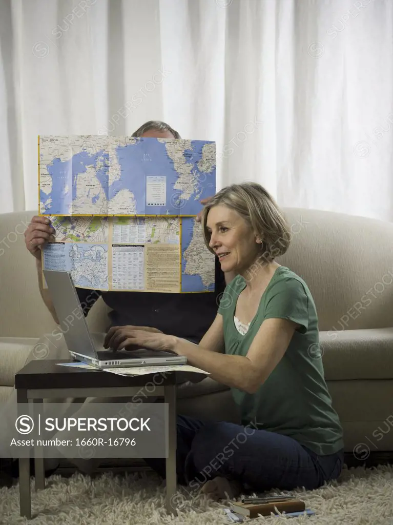 Elderly woman sitting in front of a laptop with an elderly man holding a map