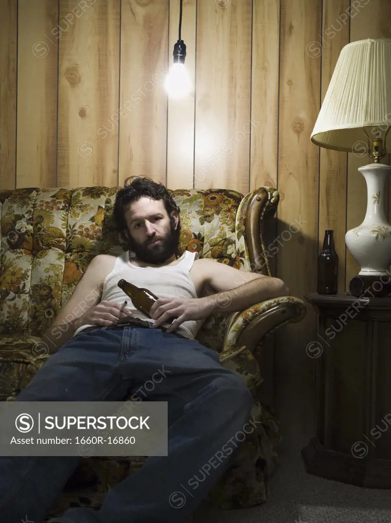 Man sitting on sofa with cigarette and beer bottle