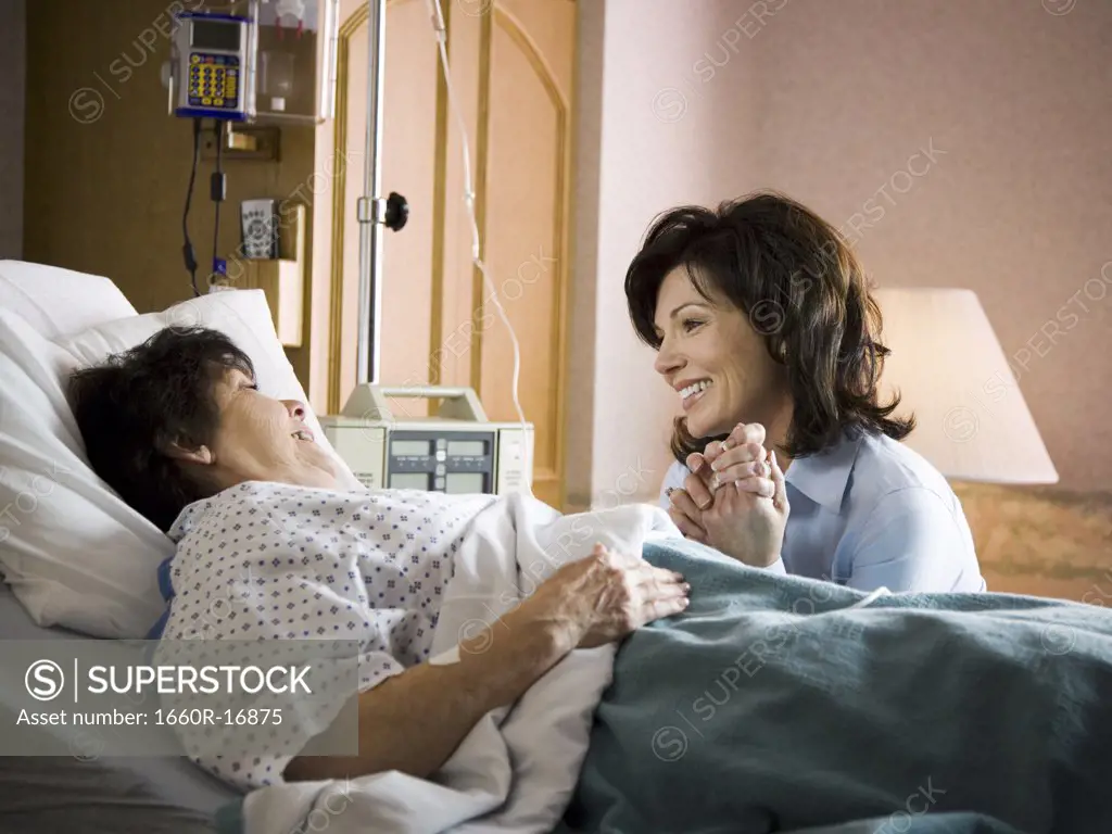 Older woman in hospital holding hands with woman smiling