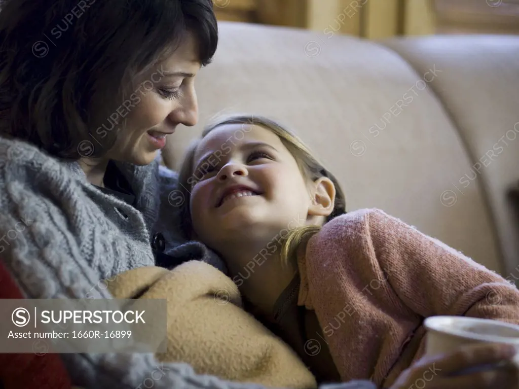 Woman with young girl snuggling on sofa
