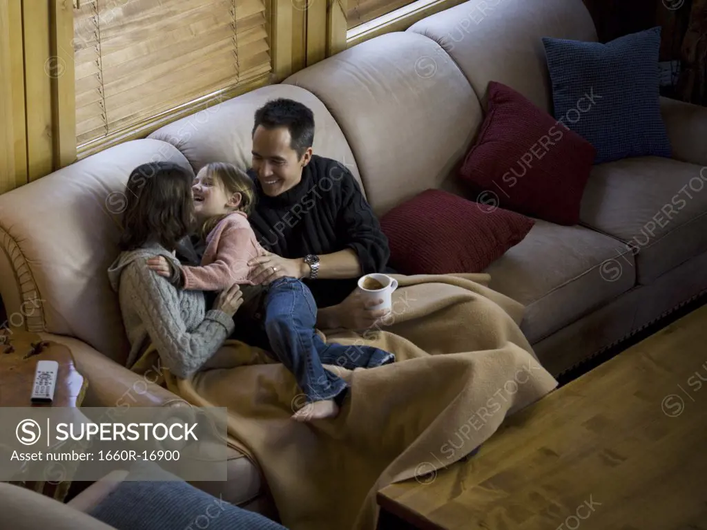 Woman and man snuggling with young girl on sofa