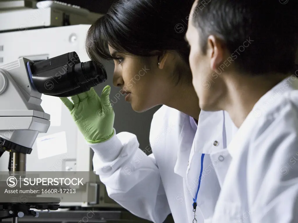 Female lab technician looking through microscope with male technician