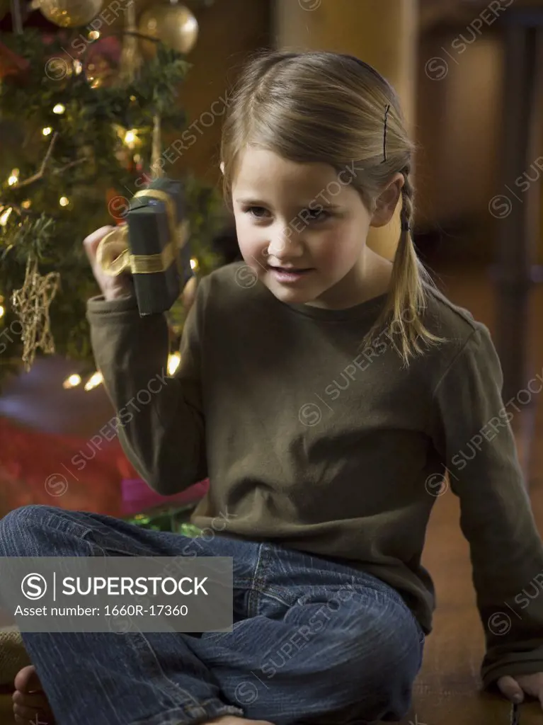 Girl shaking Christmas present with tree