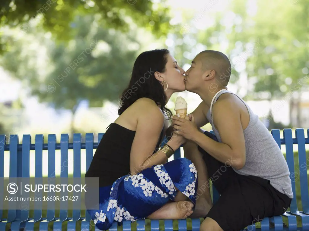 Couple kissing on park bench with ice cream cone