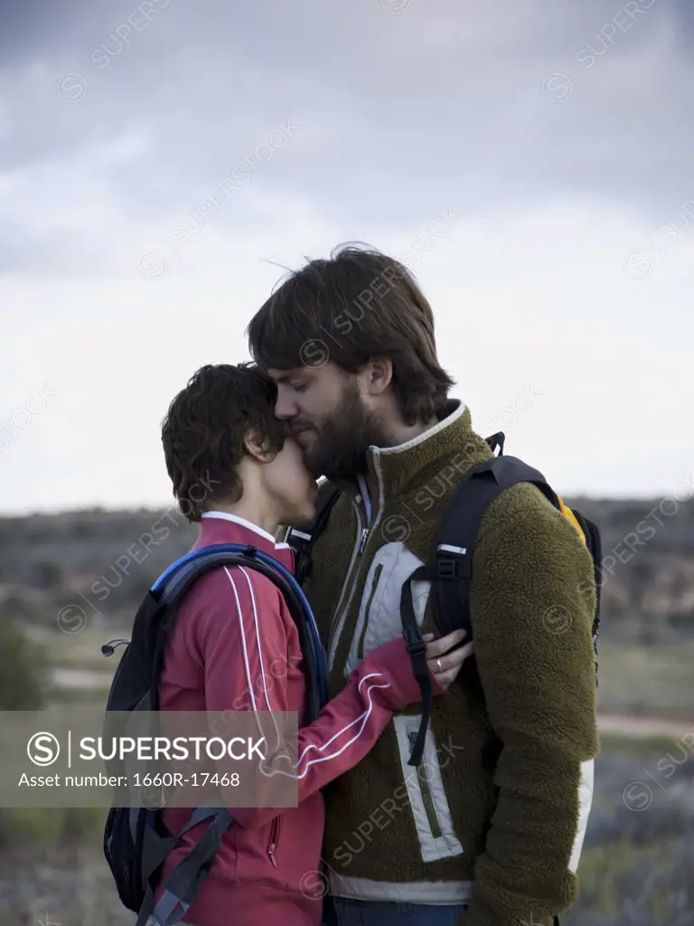 Man and woman with backpacks embracing outdoors