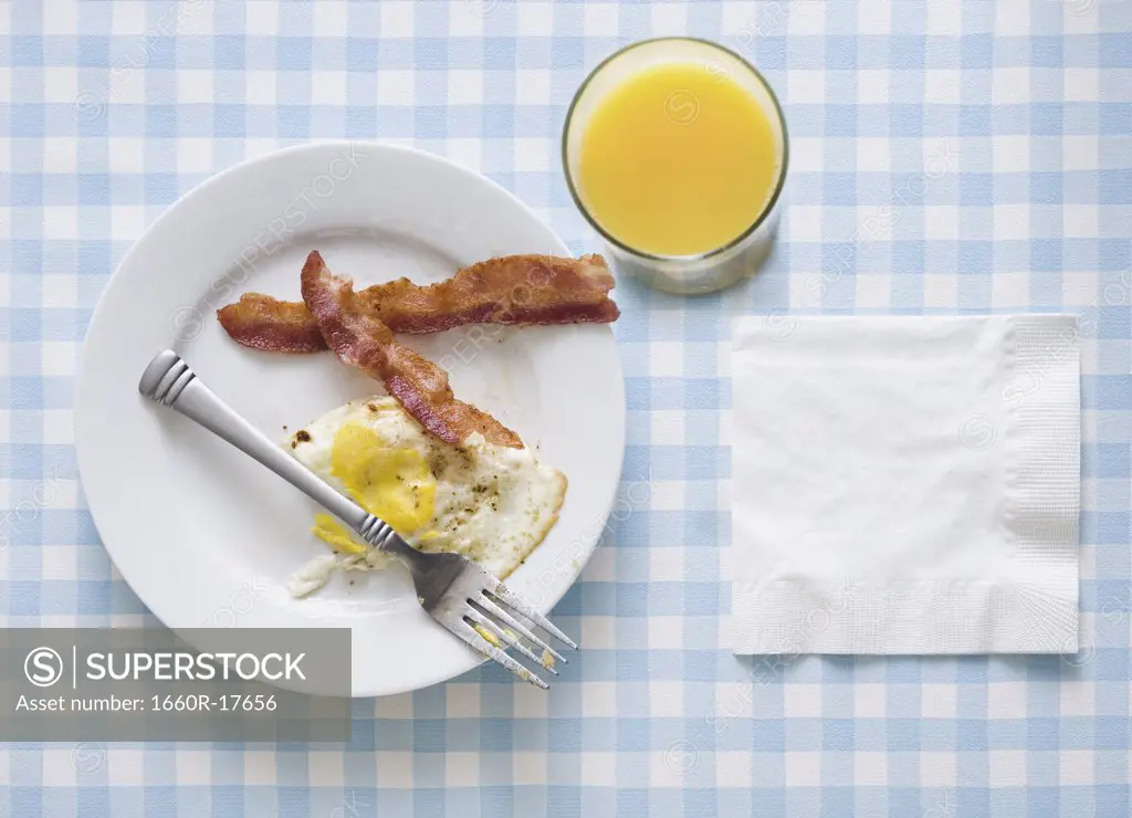 Bacon and eggs with orange juice fork and napkin