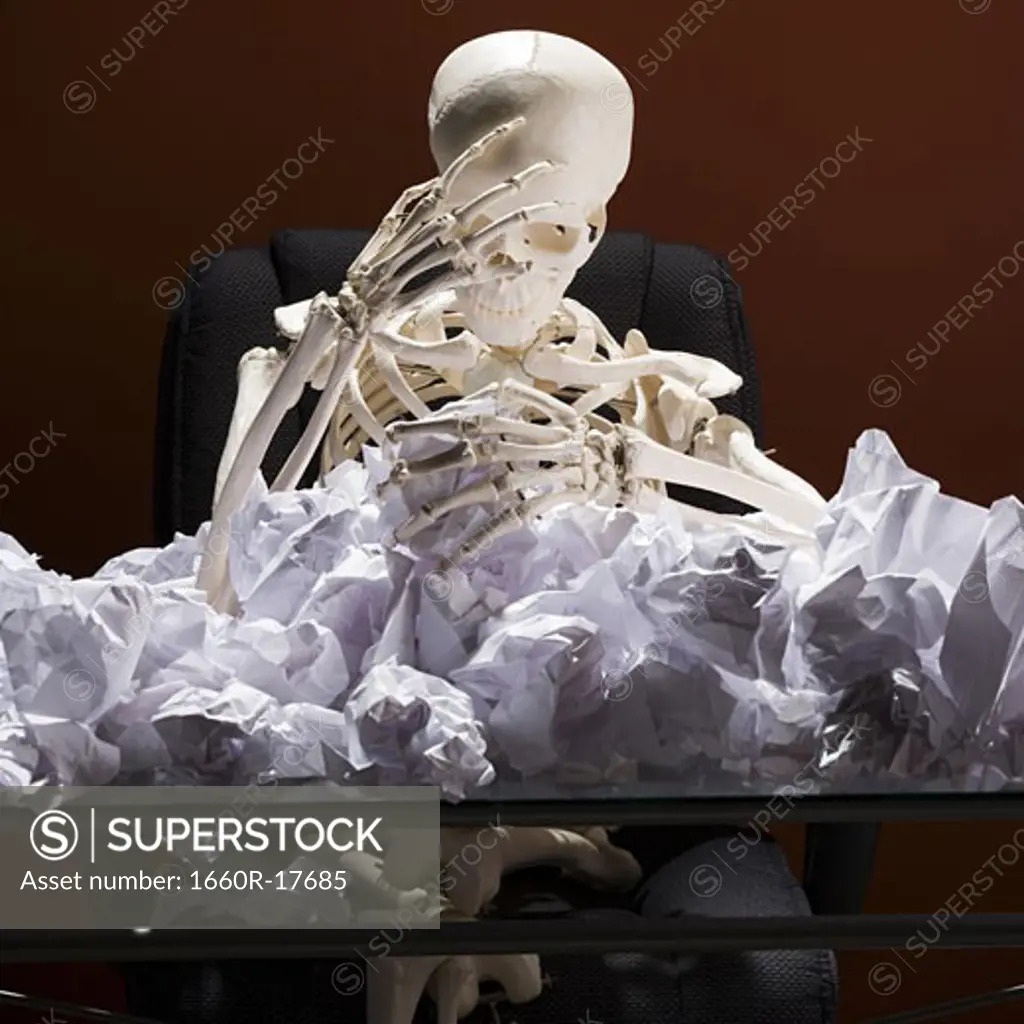 Skeleton sitting at desk with crumpled papers