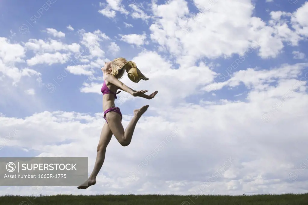 Young woman in a bikini jumping on grass