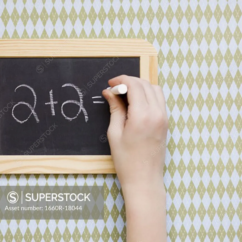 Person writing numbers on blackboard with chalk