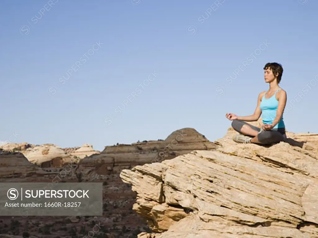 Woman sitting cross legged on rock outdoors doing yoga
