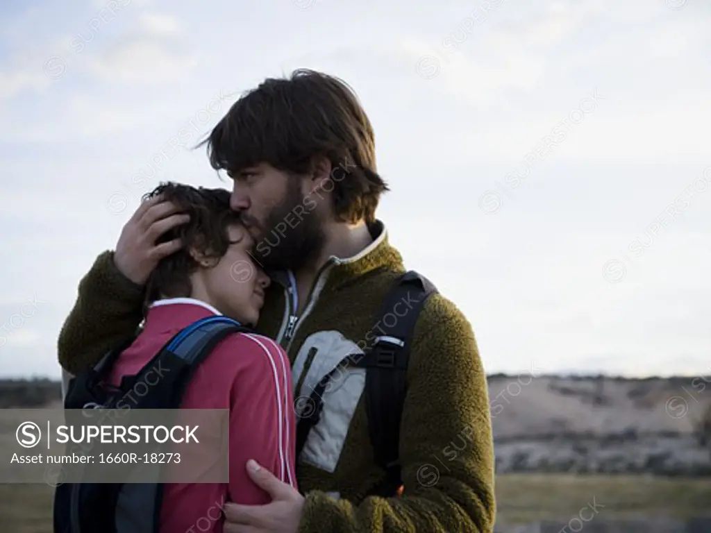 Man and woman with backpacks embracing outdoors