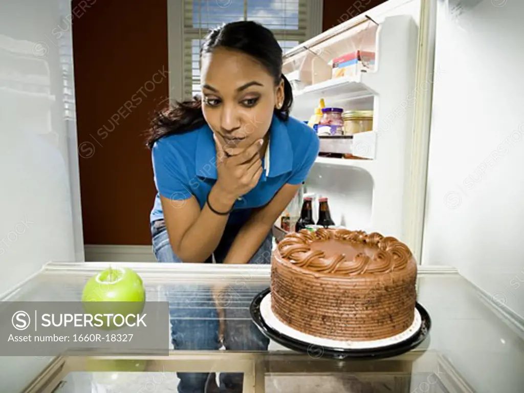 Woman in refrigerator with apple looking at chocolate cake