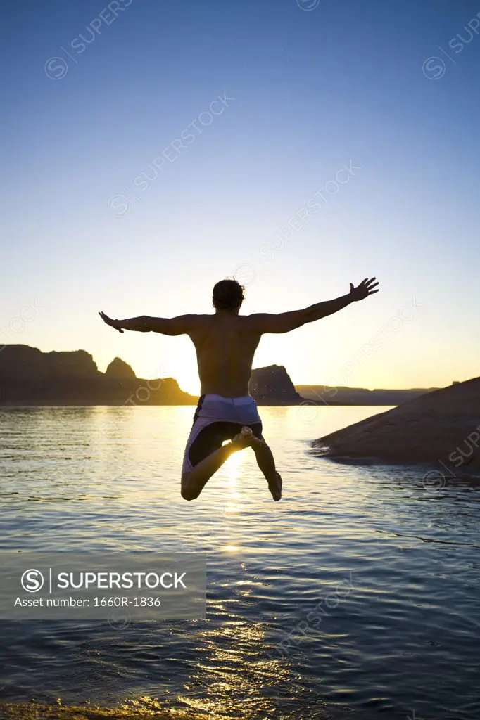 Rear view of a young man jumping into a lake
