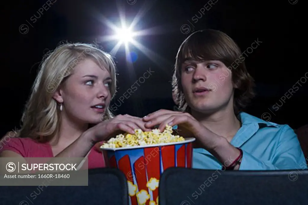 Boy and girl touching hands in popcorn at movie theater