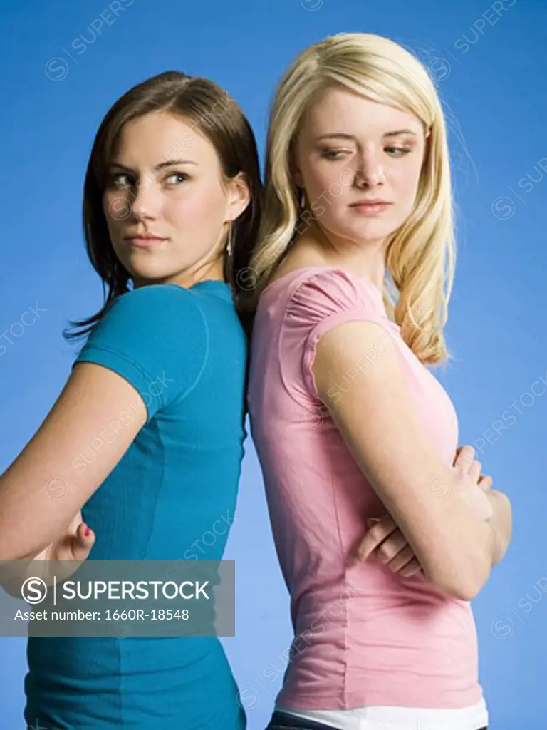 Two girls with arms crossed back to back scowling