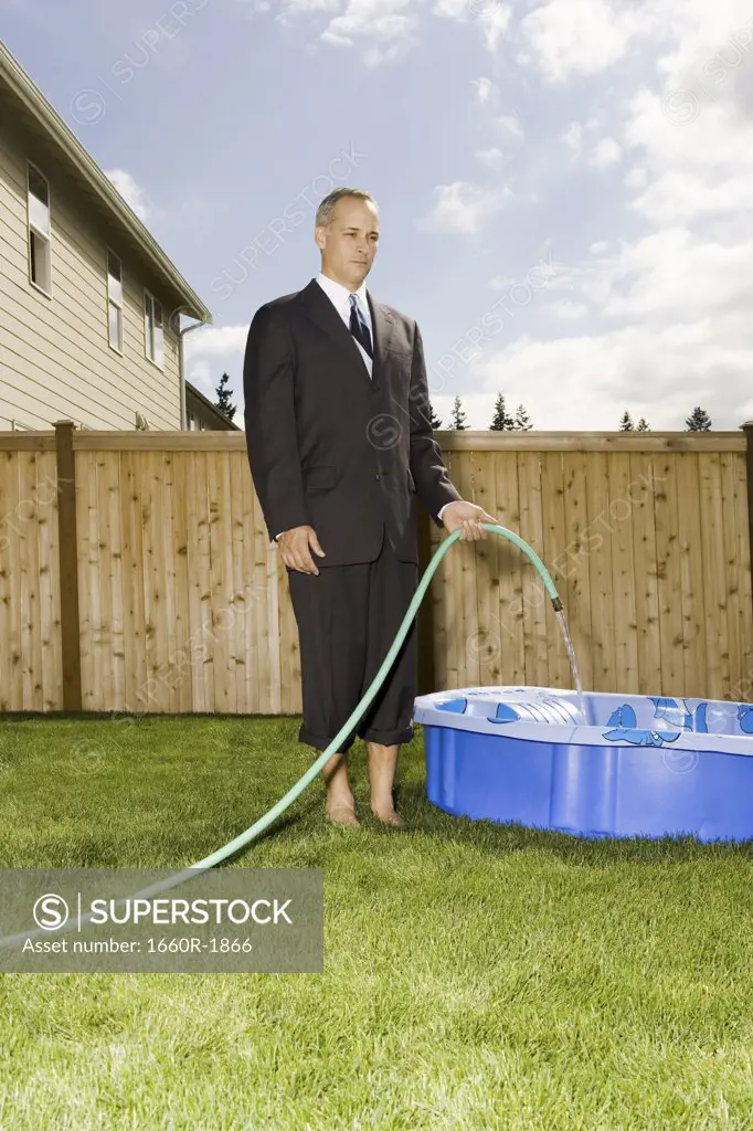 Businessman filling a wading pool with water