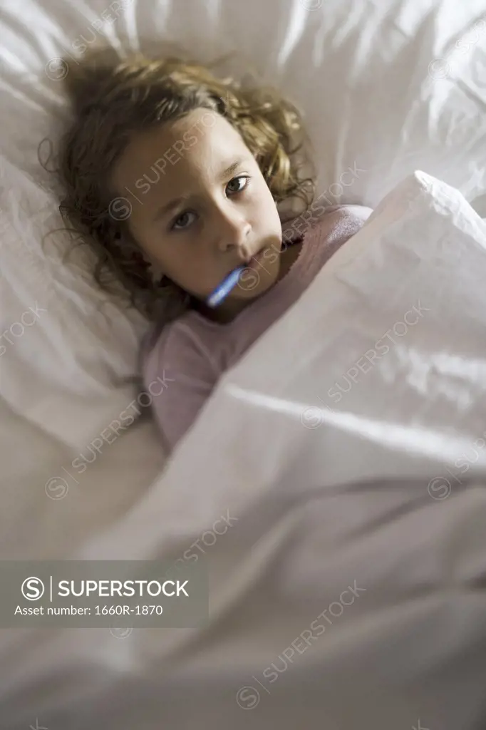 High angle view of a girl in a bed with a thermometer in her mouth